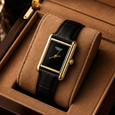 Luxury men's rectangular gold-tone watch with black dial, gold hands, and black leather strap.