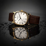 Watch with brown leather strap and gold case on a reflective surface with a dark background