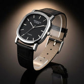 Black wristwatch with silver case and black leather strap on a white background