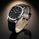 Black wristwatch with silver case and black leather strap on a white background